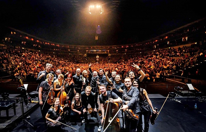 Umělci na jevišti s plným hledištěm v zádech.