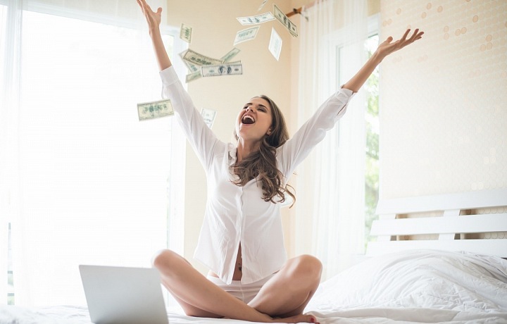 Krásná žena sedící na posteli a rozhazující peníze