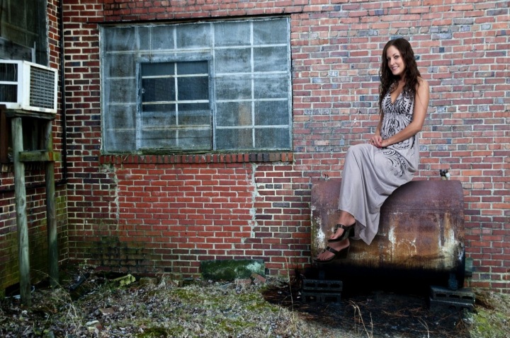 Dívka sedící před cihlovou zdí opuštěného industriálního objektu