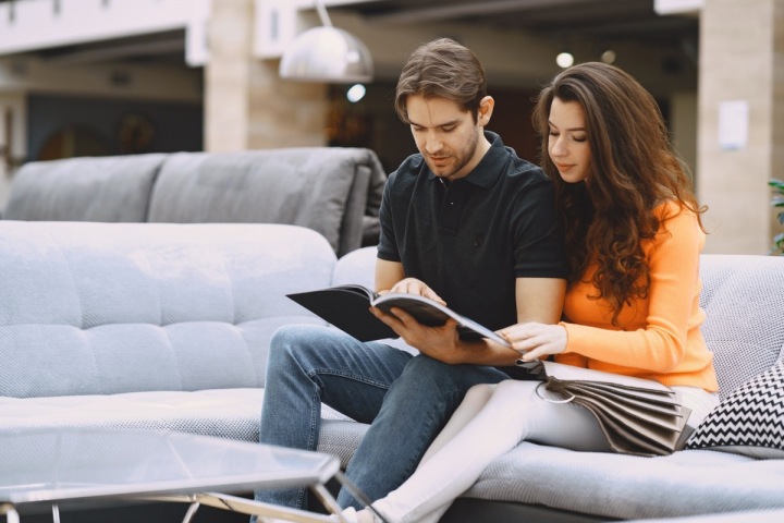 Mladý pár sedí na gauči a listuje katalogem