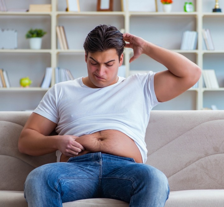 Muž s nadváhou sedí na gauči.