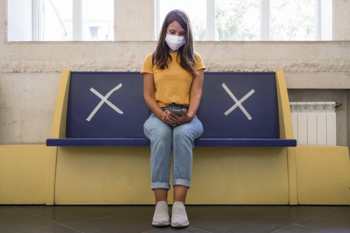 Žena s rouškou sedí na zastávce