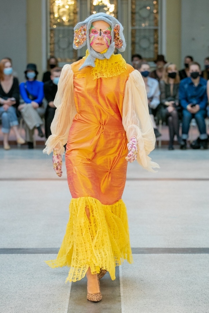 Žena v oranžových šatech a šedé čepici