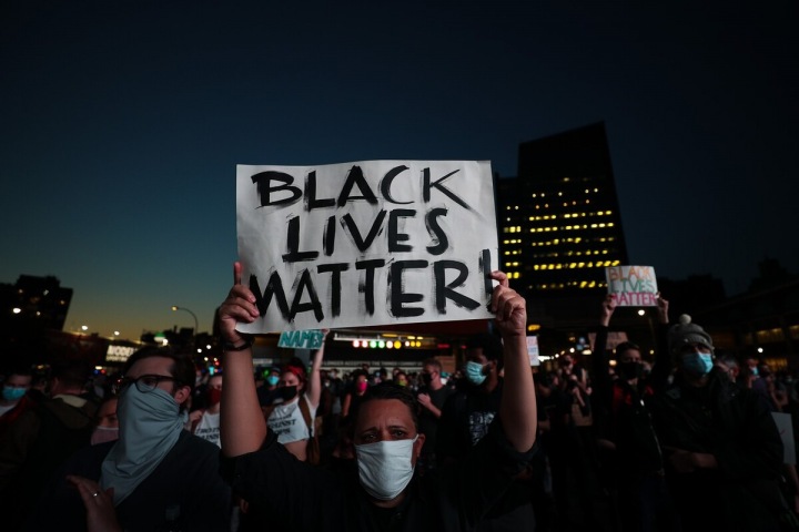 Žena v roušce drží nad hlavou plakát Black lives matter