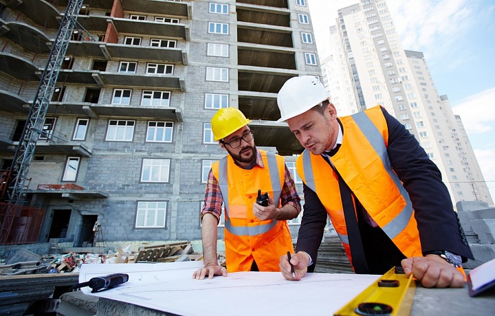 Dva stavební dělníci v oranžových vestách si prohlíží stavební plány