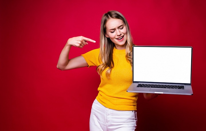 Smějící se mladá dívka ukazuje na laptop v ruce