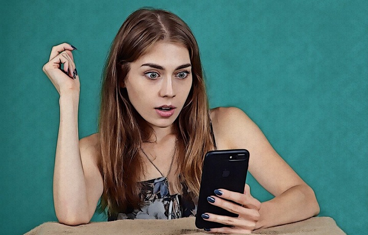 Mladá žena koukající šokovaná do telefonu.