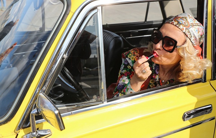 Žena se líčí v retro autě. 